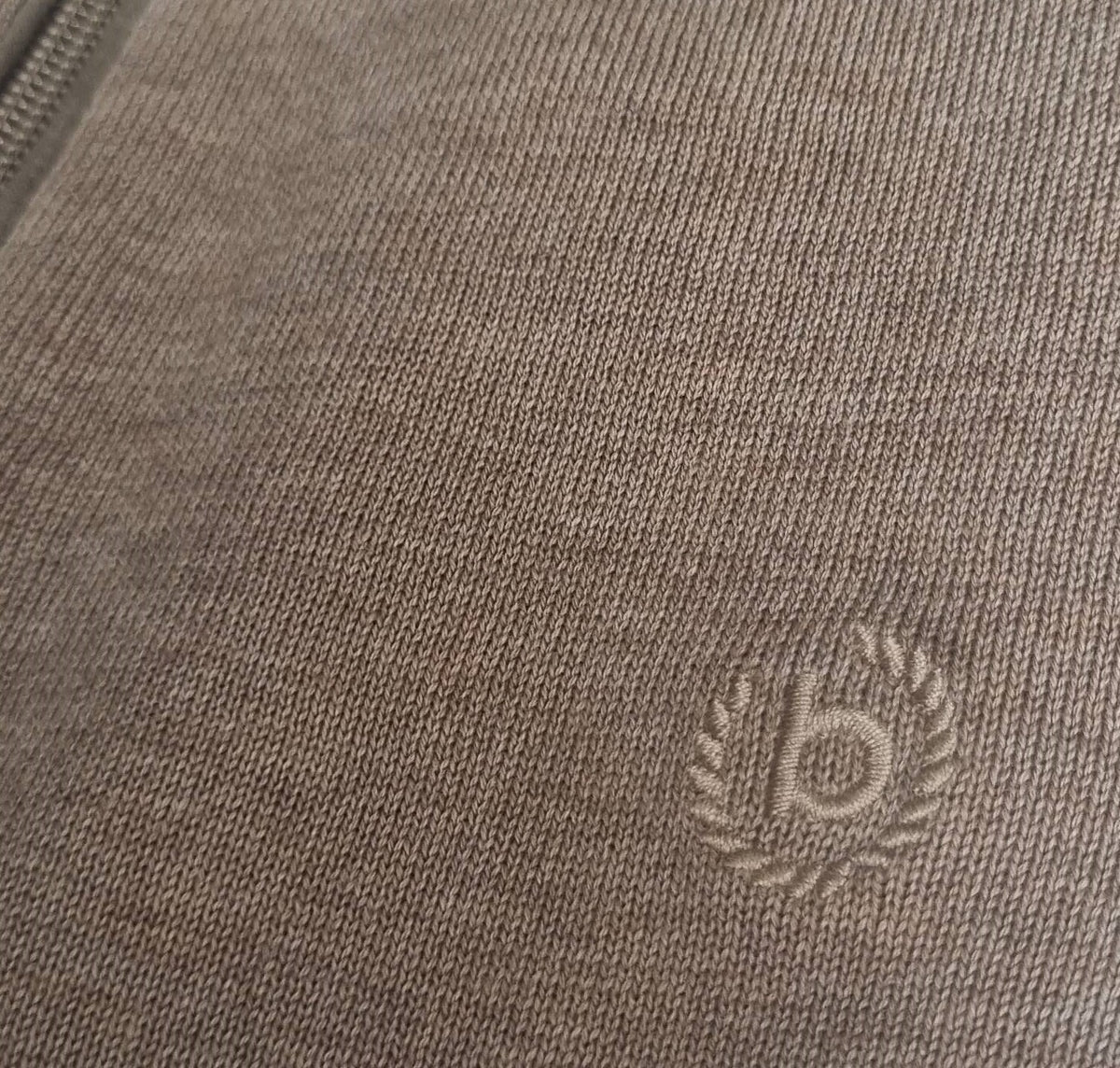 Close-up of a textured fabric surface with an embroidered logo on a product, likely a jacket or coat.
