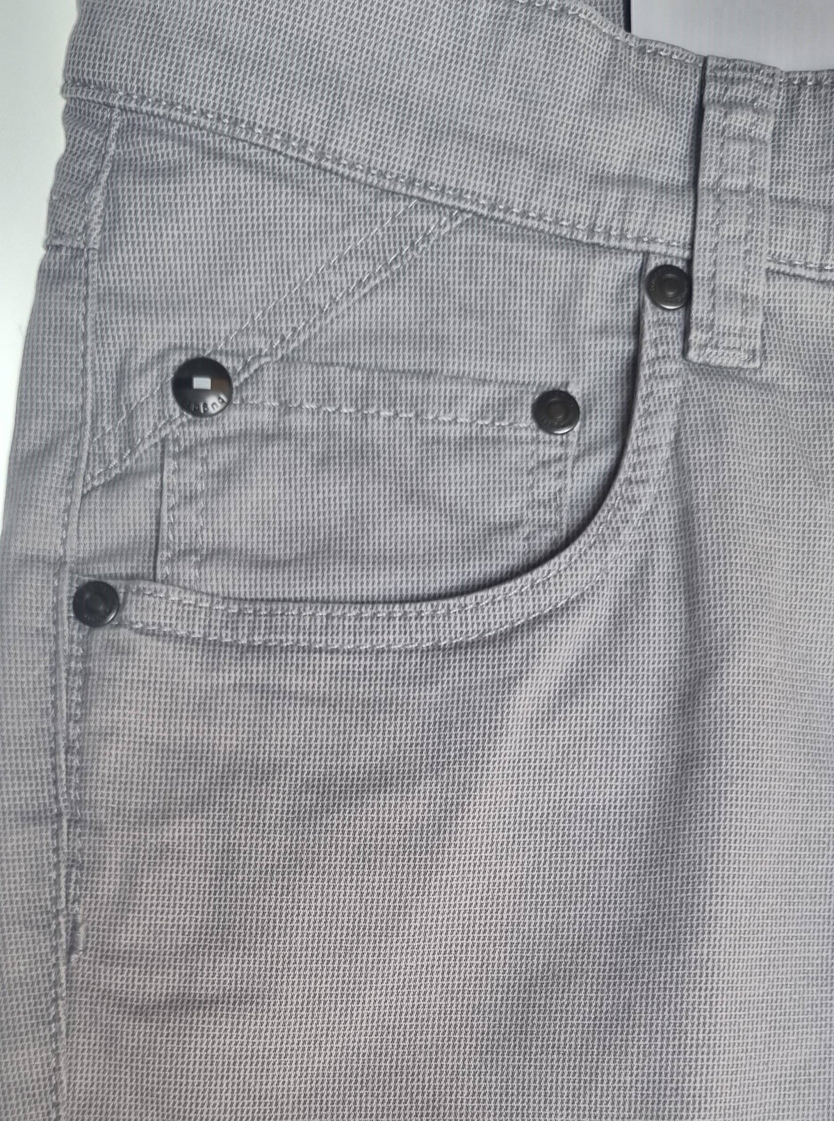 Close-up of gray pants with button details on a plain background
