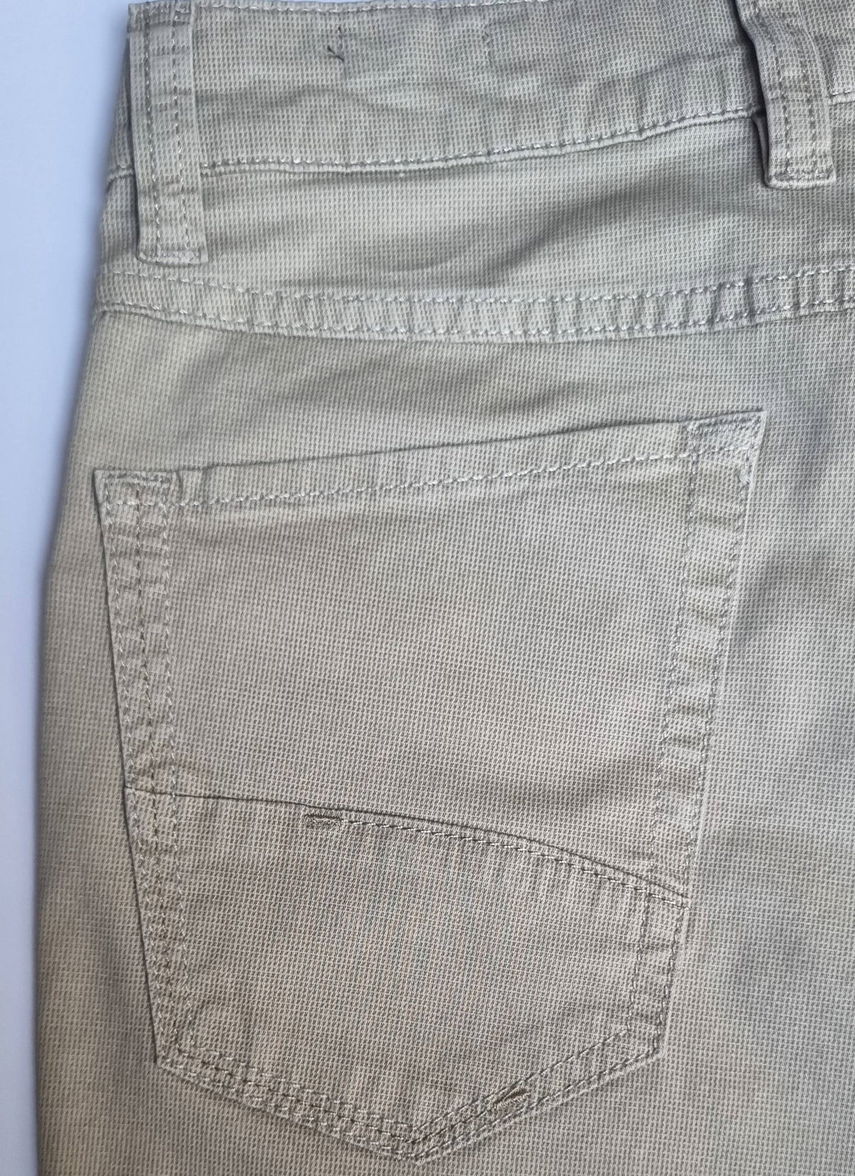 Close-up of a pocket on a pair of beige pants with a light blue background