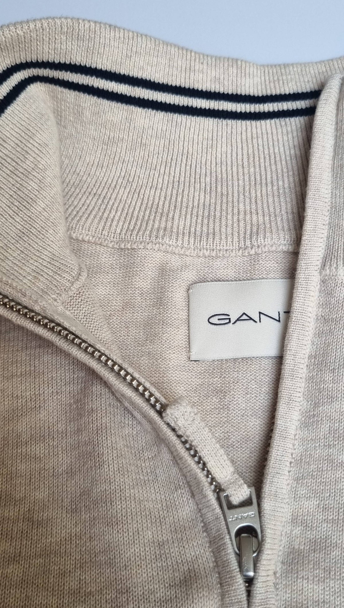 Close-up of a Gant brand label on a gray garment with a zipper.
