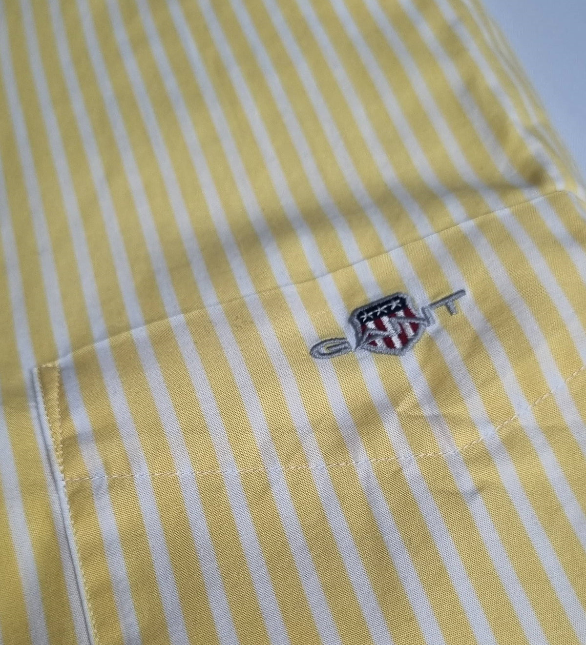 Close-up of a yellow and white striped shirt with a logo on the chest pocket.