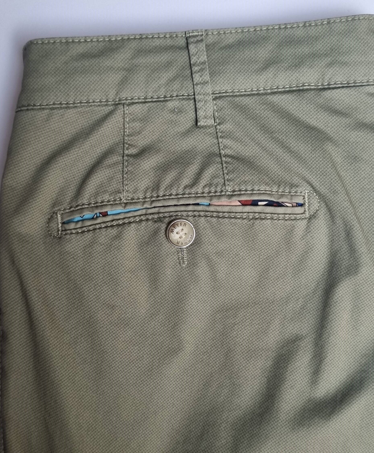 Close-up of green pants with a button and floral pattern on the back pocket.